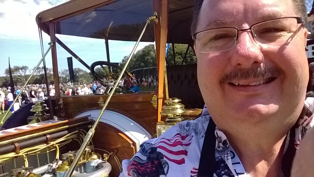 A man in glasses and an american flag shirt is smiling.