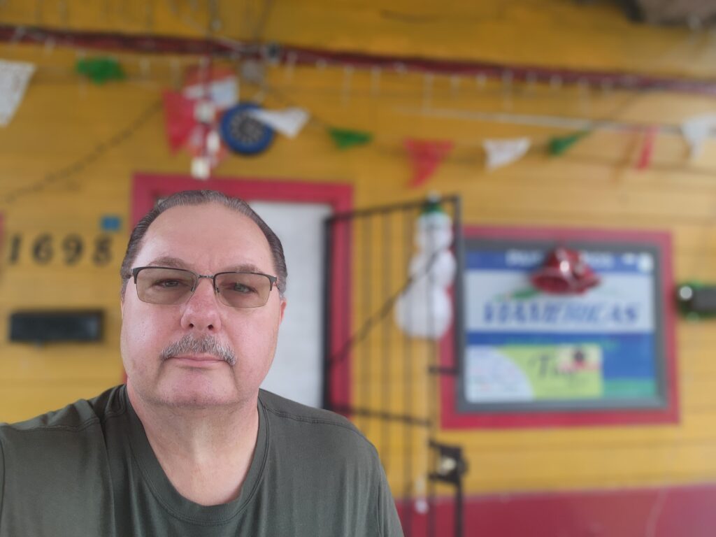 A man with glasses standing in front of a yellow wall.