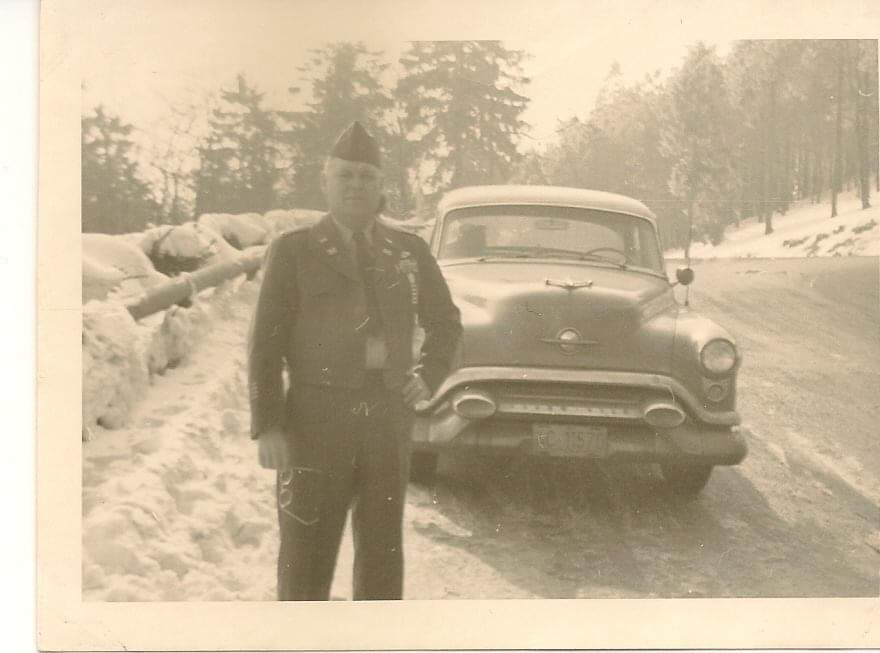 A man in uniform standing next to an old car.