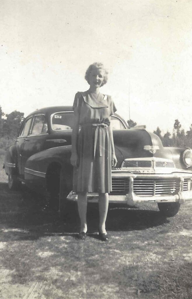 A woman standing in front of an old car.