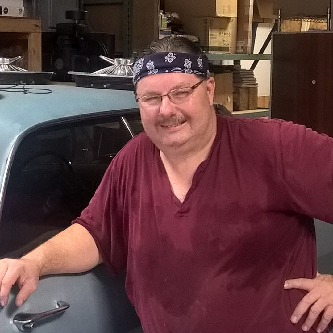 A man standing next to a car in a garage.